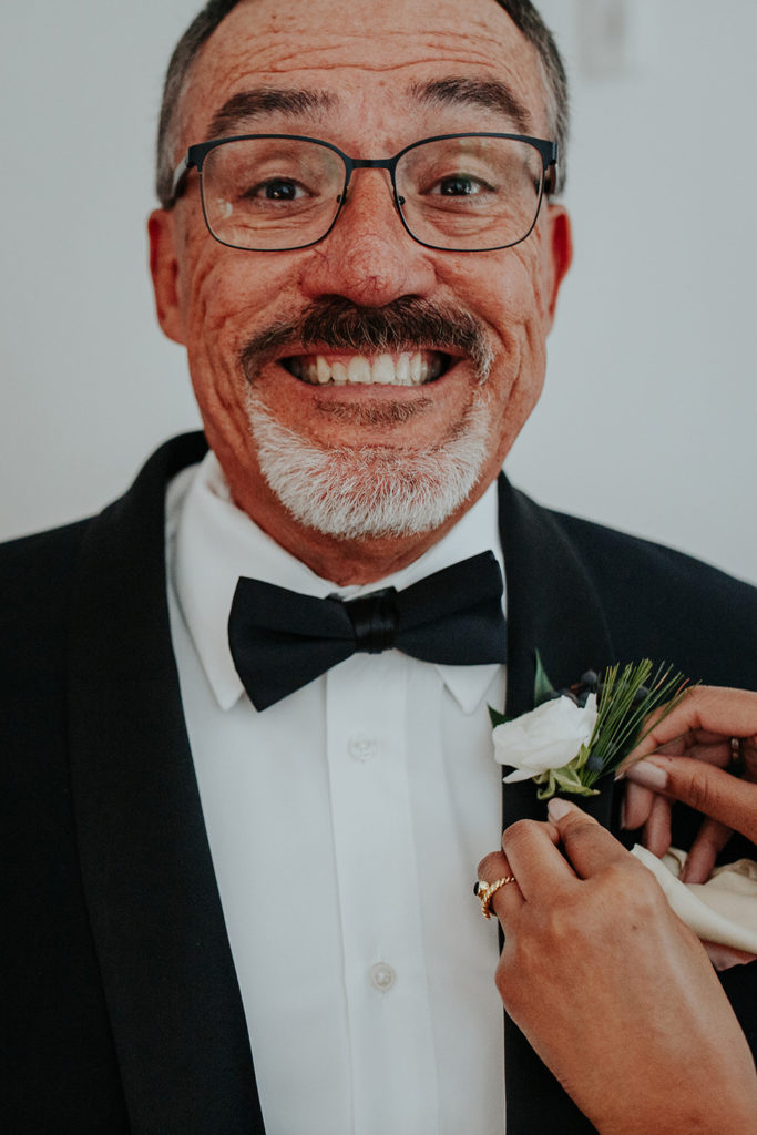 Father of the groom grins as his boutonniere is pinned before ceremony