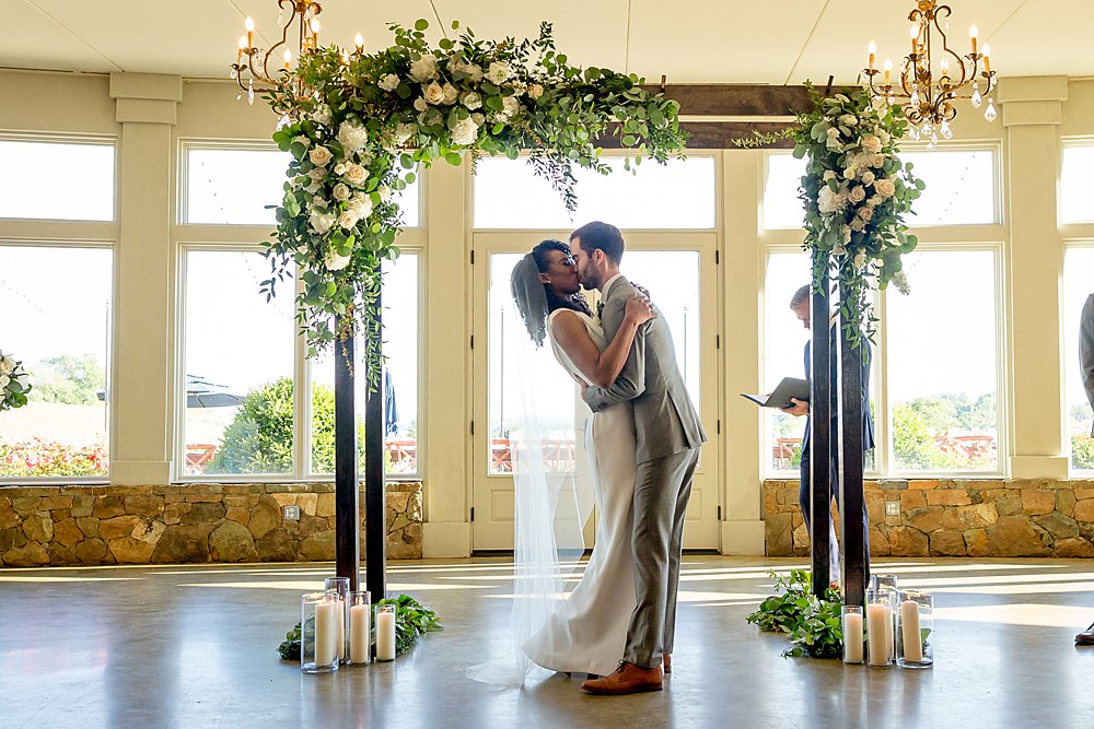 Couple exchanging a kiss at the end of their ceremony, with arch in background